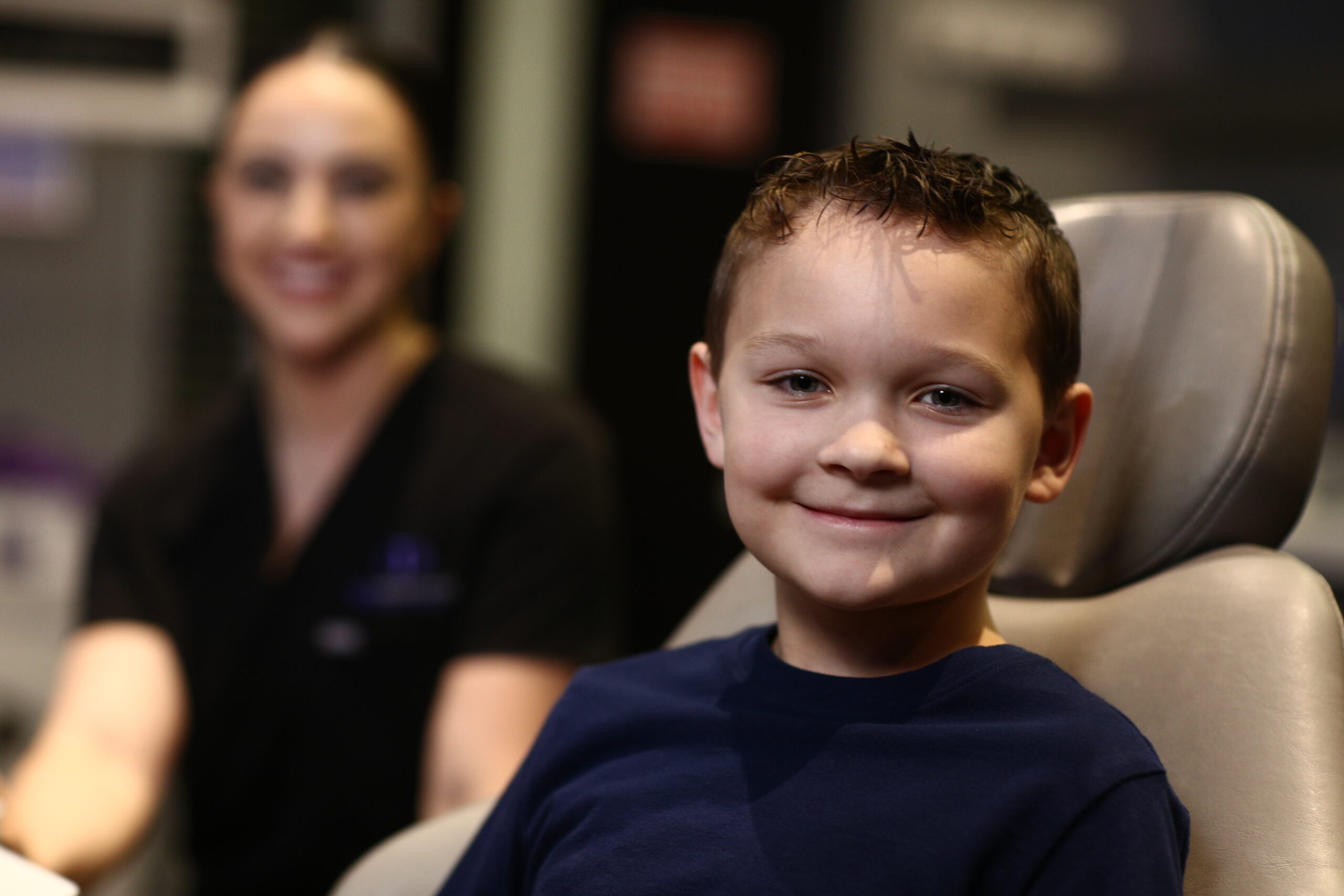 Smiling boy in orthodontic chair with dental professional blurred in background, highlighting friendly orthodontic care at Icon Orthodontics.