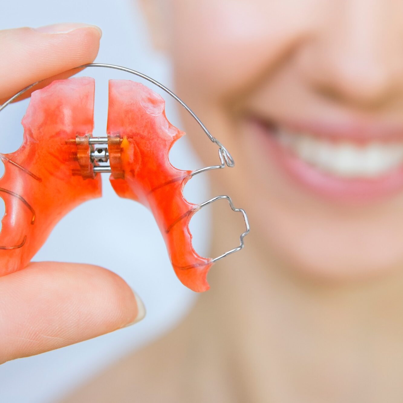 Removable orthodontic retainer held by a smiling individual, highlighting its importance in maintaining dental alignment post-braces.